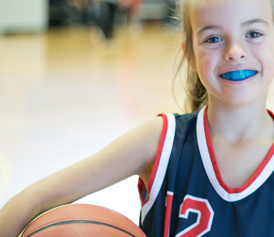 girl posing with basketball wearing a blue custom mouthguard
